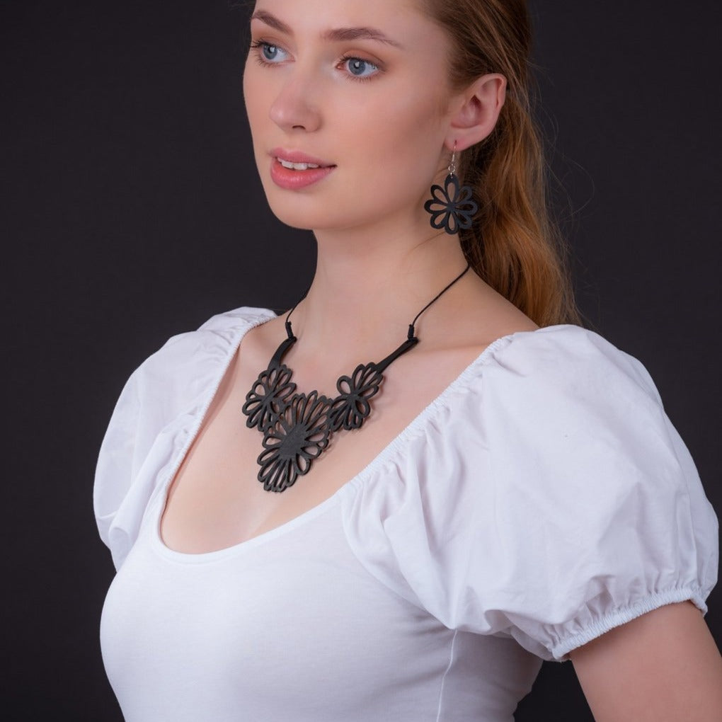 Paguro Upcycle black floral upcycled inner tube necklace worn by woman in white puff sleeve top