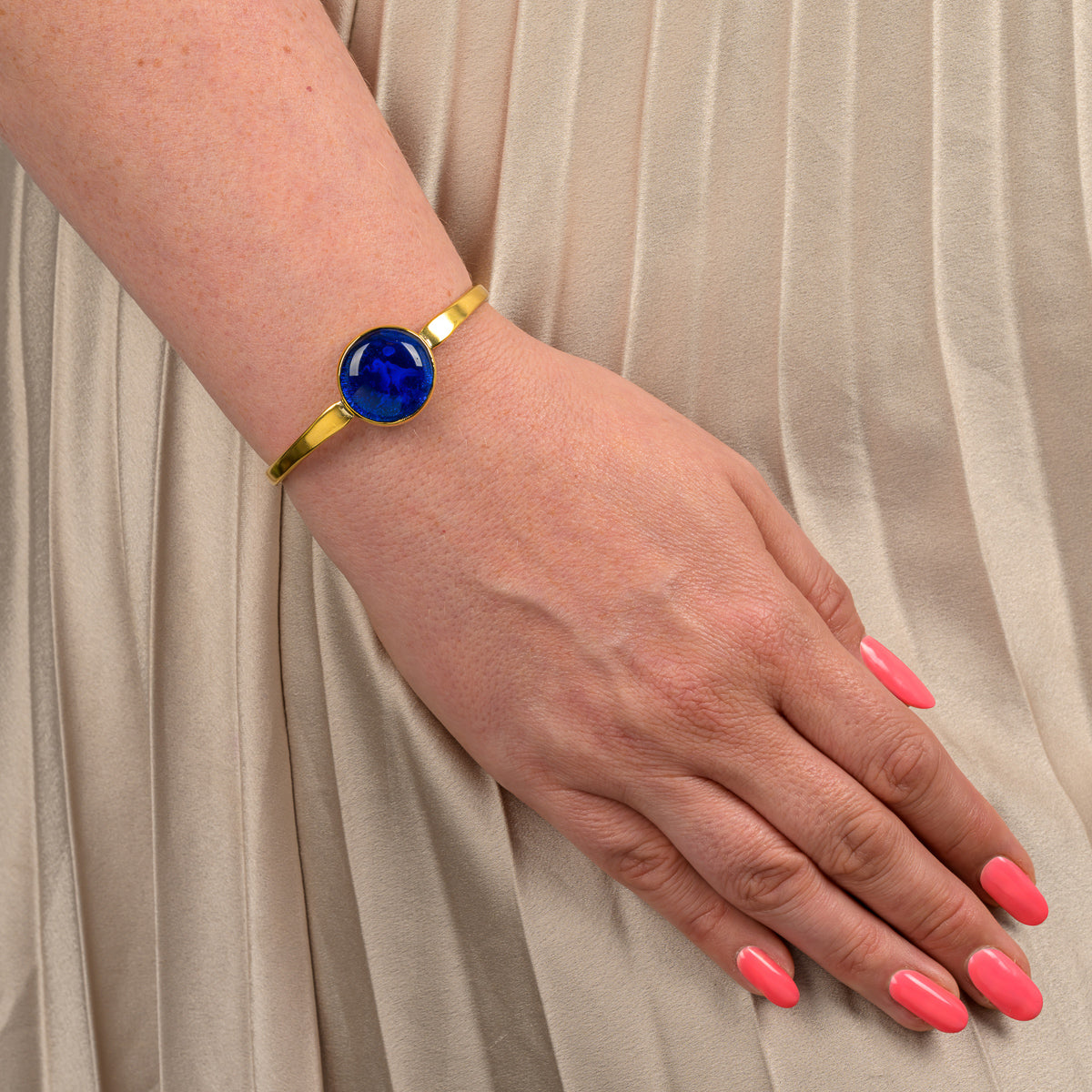 Paguro Upcycle recycled brass bangle with blue stone worn on wrist over beige pleated fabric