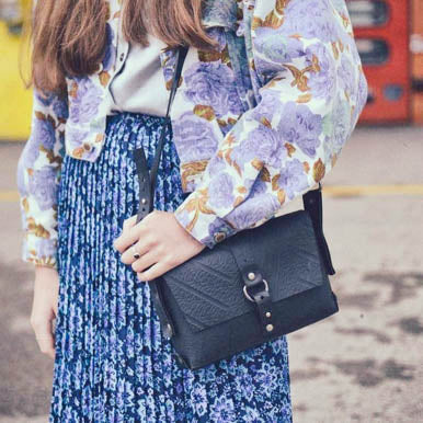 Paguro Upcycle black vegan handbag with buckle detail worn crossbody by a woman in floral and blue skirt outfit