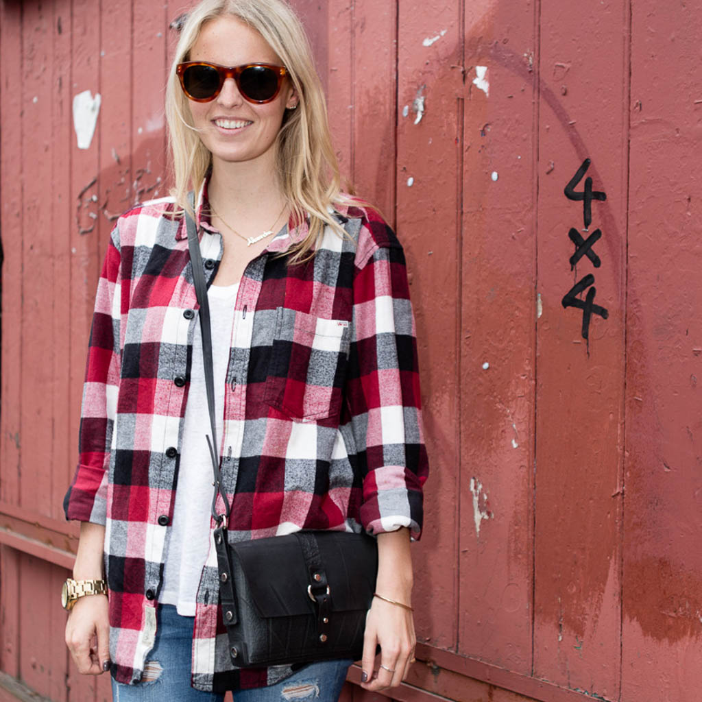 Woman wearing a red plaid shirt and sunglasses carrying a black vegan handbag by Paguro Upcycle