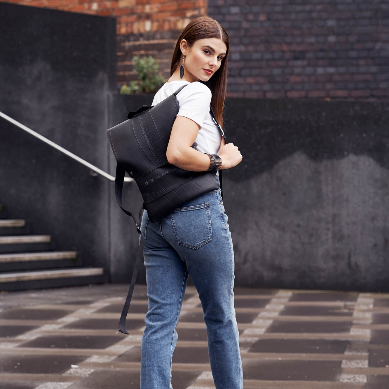 Woman wearing Paguro Upcycle vegan inner tube backpack in black outdoors with white shirt and jeans